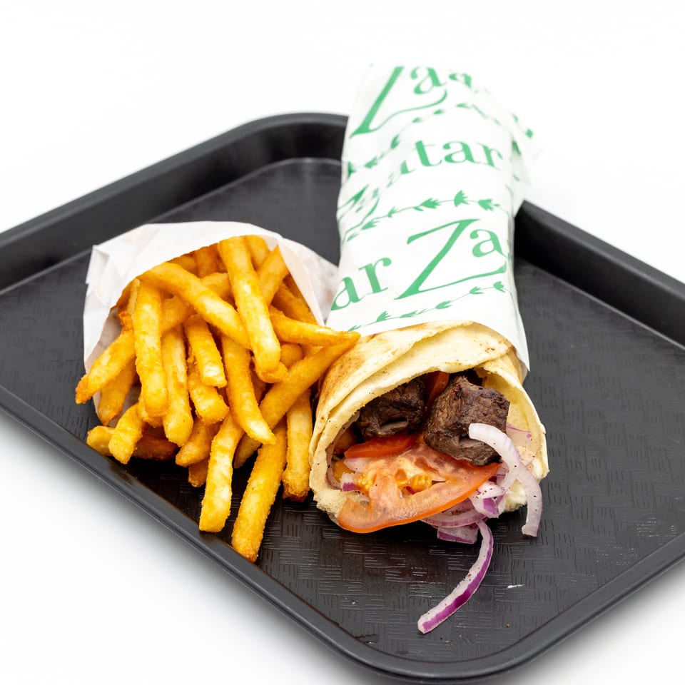 Gyro wrap with grilled meat, tomatoes, onions, and fries served on a black tray.