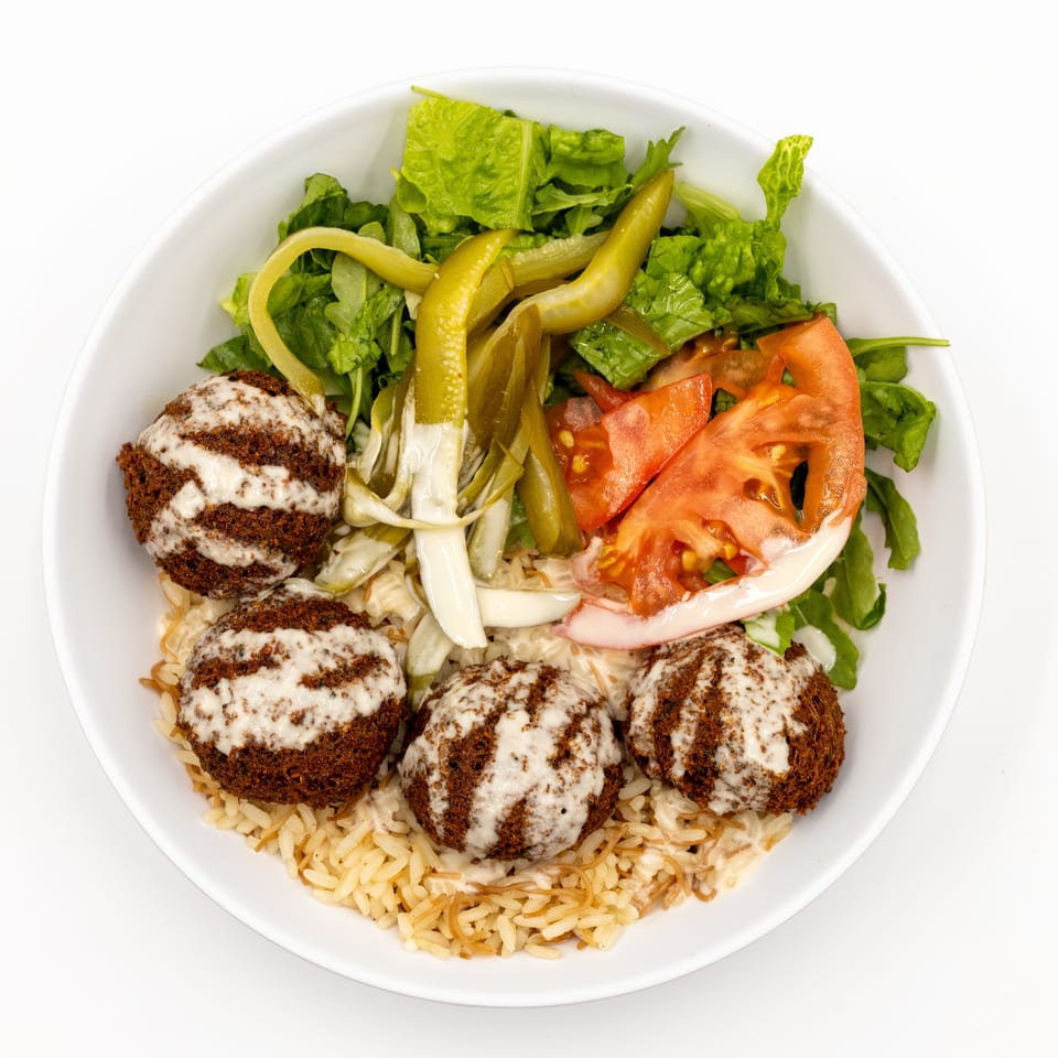Bowl of rice topped with falafel, tahini sauce, lettuce, tomatoes, pickled peppers, and onions.