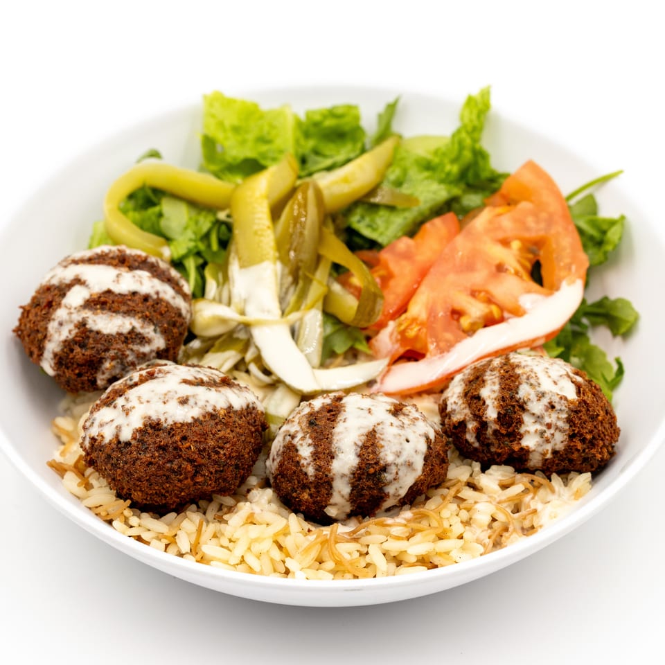 Falafel balls drizzled with tahini over rice, served with lettuce, tomatoes, cucumbers, and pickled peppers.