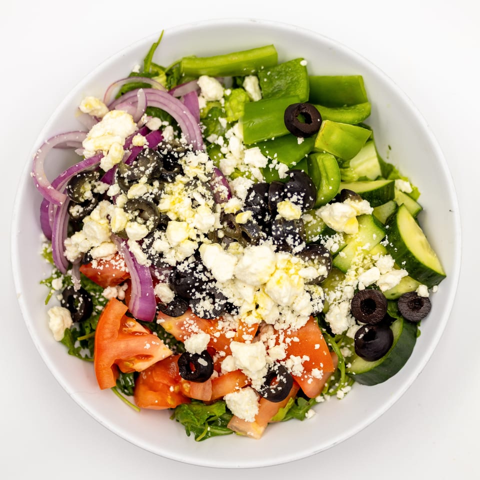 Overhead view of a Greek salad with lettuce, tomatoes, cucumbers, green peppers, red onions, olives, and feta cheese.