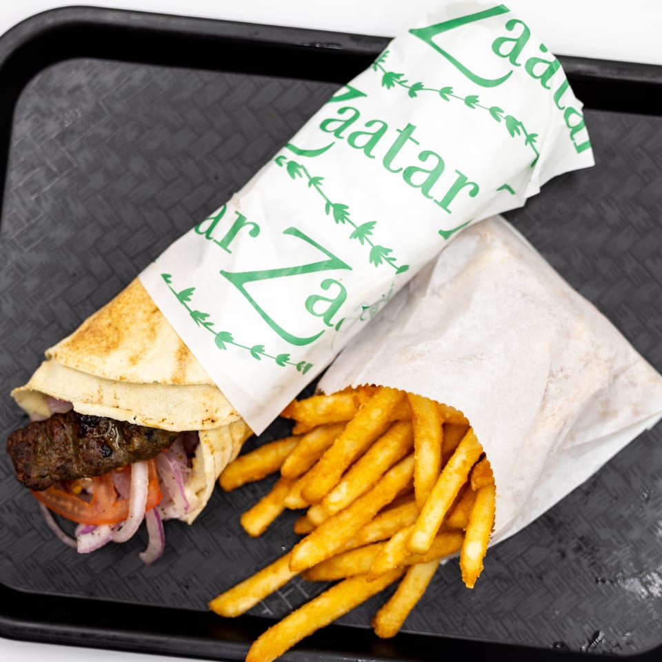 A grilled meat pita sandwich with vegetables and golden fries served on a black tray.