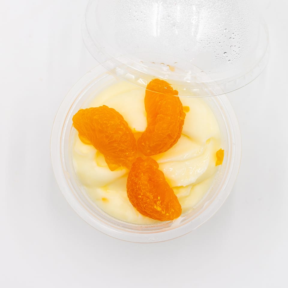 Open plastic container holding creamy white dessert topped with several bright orange fruit segments.
