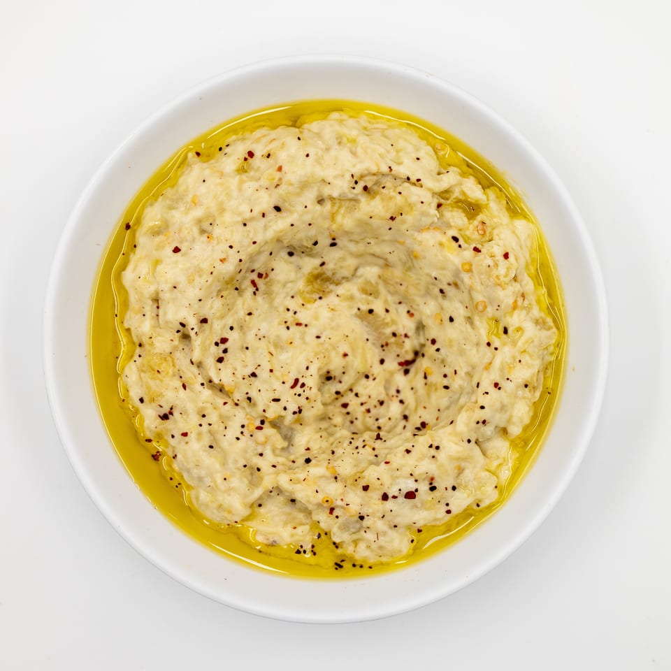 Creamy hummus topped with red pepper flakes and olive oil in a white bowl.