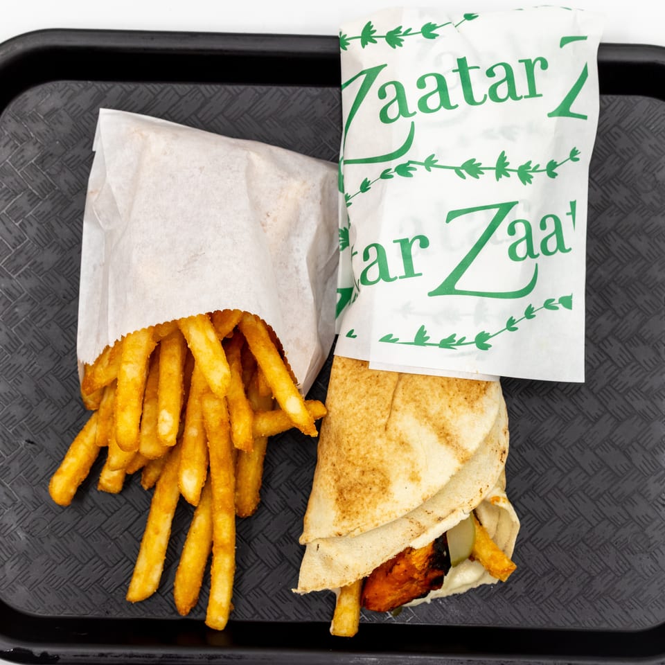 Zatar-wrapped grilled chicken sandwich with fries on a black serving tray.