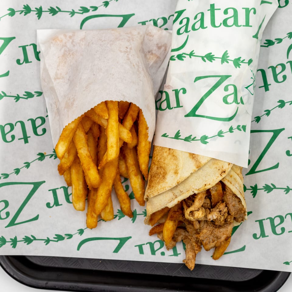 Overhead view of seasoned fries and a stuffed pita wrap on branded paper in a black serving tray.