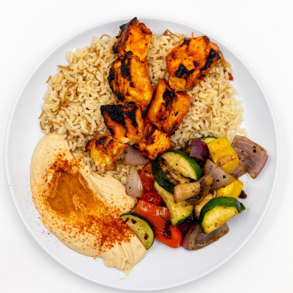 Plate of grilled chicken, rice, hummus, and roasted zucchini, peppers, onions, and mushrooms.