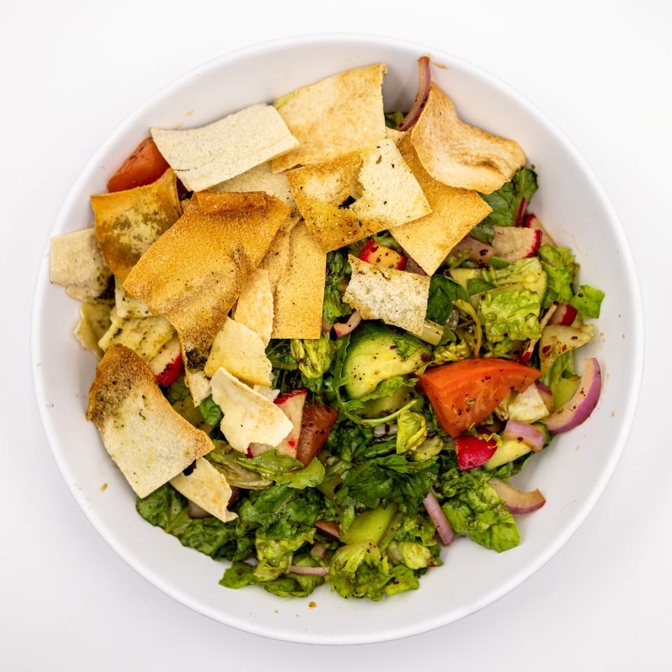 Top-down view of a fresh chopped salad with lettuce, tomatoes, cucumbers, radishes, onions, and toasted pita pieces.